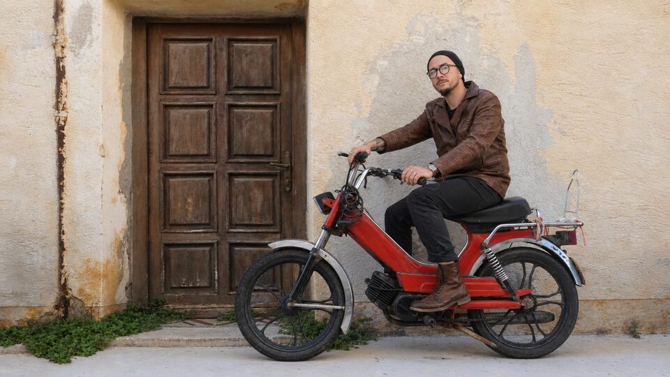 Un conducteur assis sur un cyclomoteur devant une porte ancienne